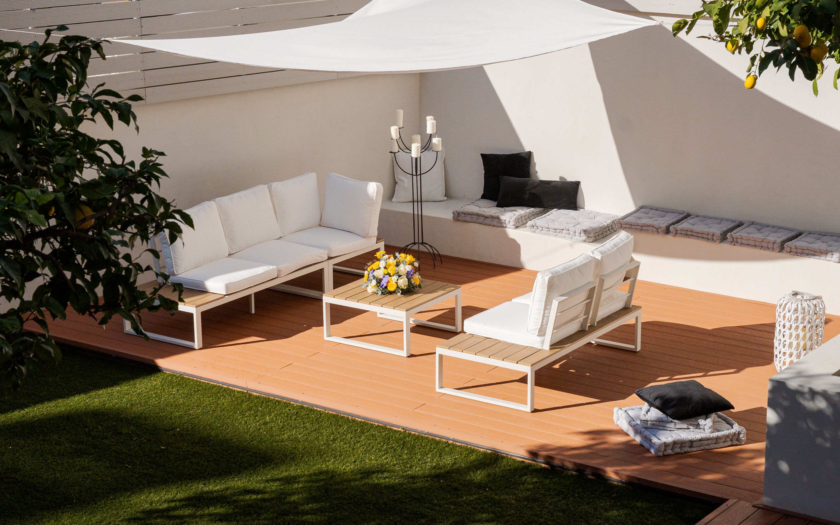 Une terrasse extérieure avec un canapé blanc, une table basse en bois agrémentée de fleurs et un fauteuil blanc.