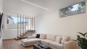 Una sala de estar moderna con un sofá beige, una mesa de centro de mármol oscuro y una escalera con barandilla.