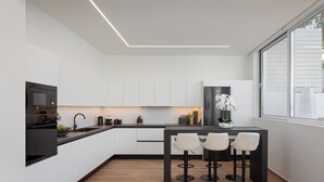 Una cocina moderna con armarios blancos, encimera negra y una zona de comedor con tres taburetes blancos.