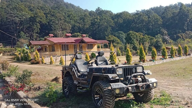 A rustic lodge with a red roof, surrounded by a well-maintained garden and a row of coniferous trees. - River View Bamboo Resort (Lansdowne)