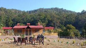 A wooden house with a red roof, surrounded by a garden with small plants and a table with chairs. - River View Bamboo Resort (Lansdowne)