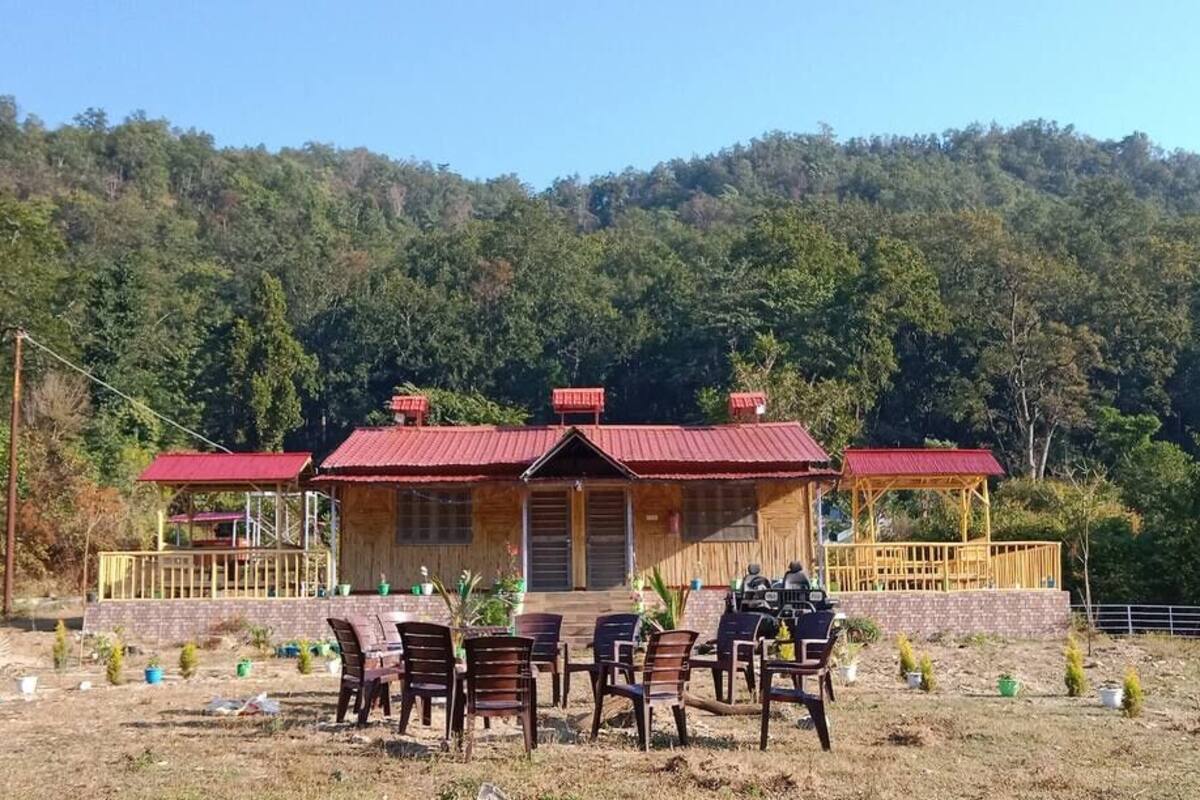 Una casa in legno con tetto rosso, circondata da un giardino con piccole piante e un tavolo con sedie.