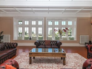 A spacious room with a large window, a leather sofa, a wooden coffee table, and a patterned rug. - Alston Hall (Plymouth)
