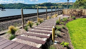 A wooden deck leading to a seating area with a view of a lake and hills. - Britannia Crossings Cottage (Dartmouth)