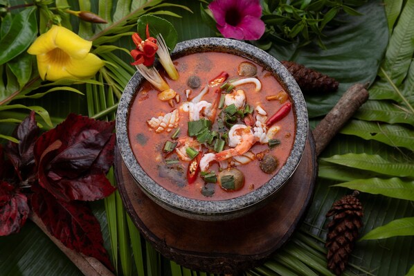 A bowl of soup with shrimp and herbs, surrounded by green leaves and flowers. - Romdoul Kirirom Resort by EHM (Kampong Seila)