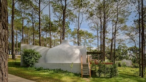 A modern building with a unique, rounded roof structure surrounded by a forested area. - Romdoul Kirirom Resort by EHM (Kampong Seila)