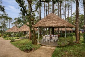 Un restaurante con mesas al aire libre bajo un techo de paja, rodeado de árboles.