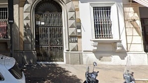 Un edificio con entrada protegida por una reja, una moto estacionada y un coche blanco.