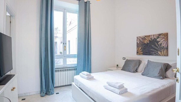 Un dormitorio con cama, televisor, ventana con cortinas y un cuadro en la pared.
