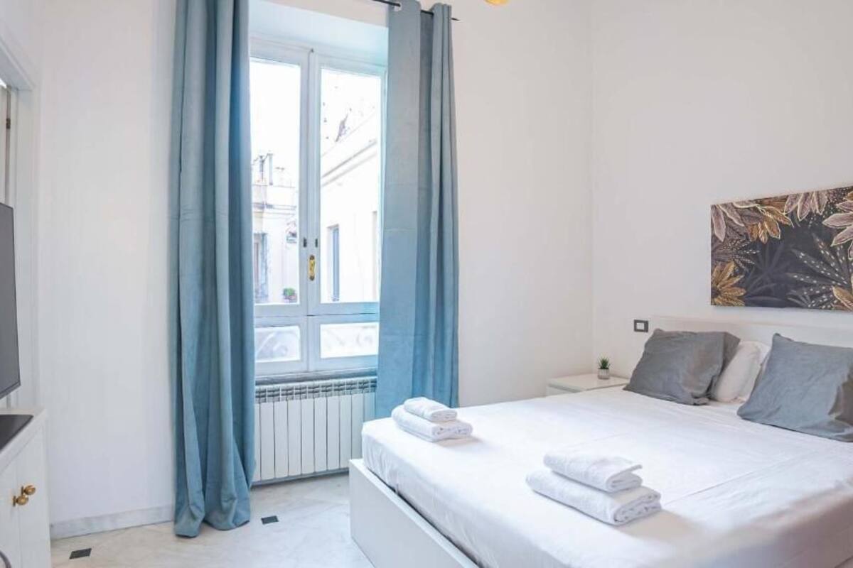 Une chambre à coucher avec un lit, une télévision, une fenêtre avec des rideaux et un tableau au mur.