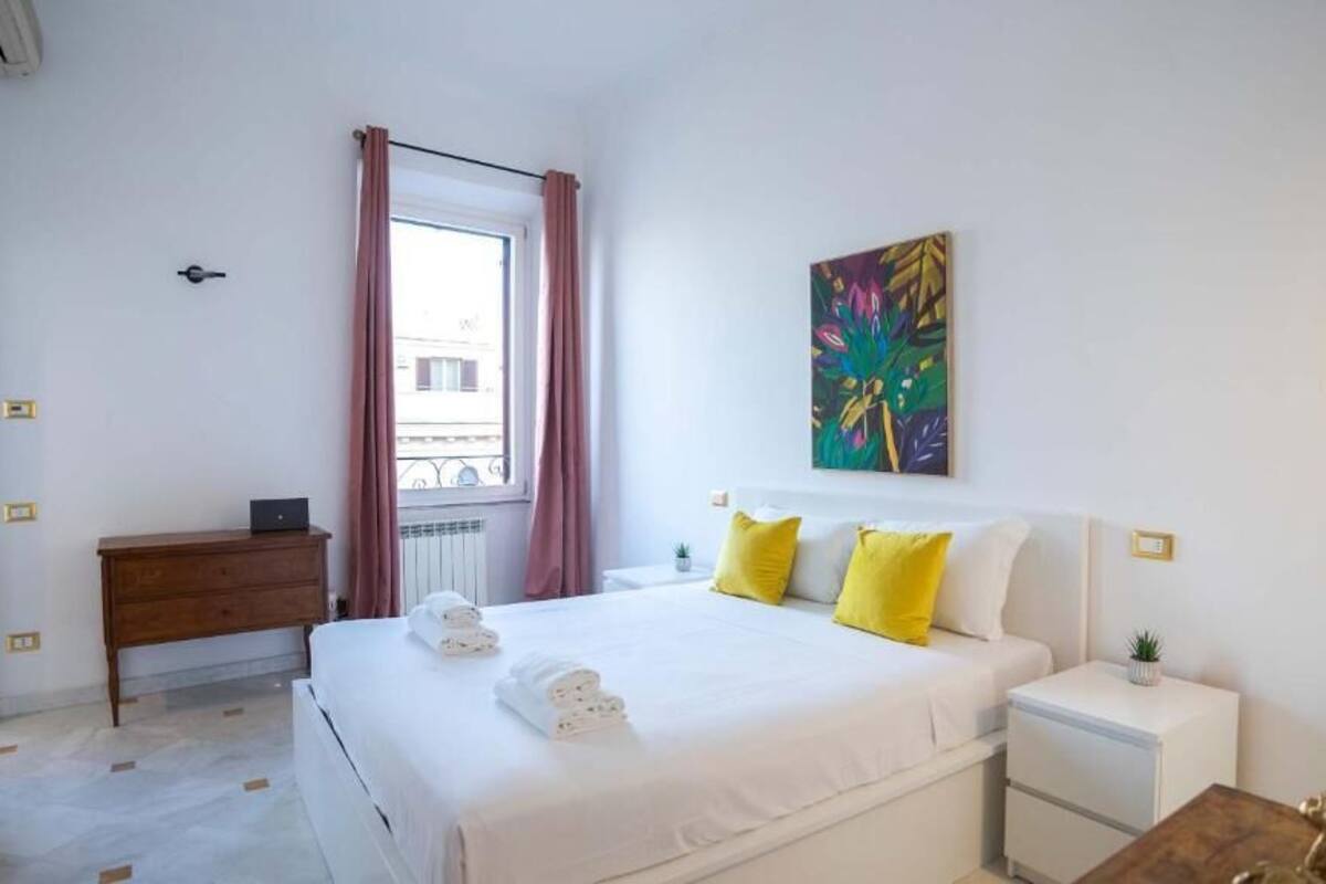 Une chambre d’hôtel avec un lit, des tables de chevet, une commode, une fenêtre avec des rideaux et un tableau au mur.