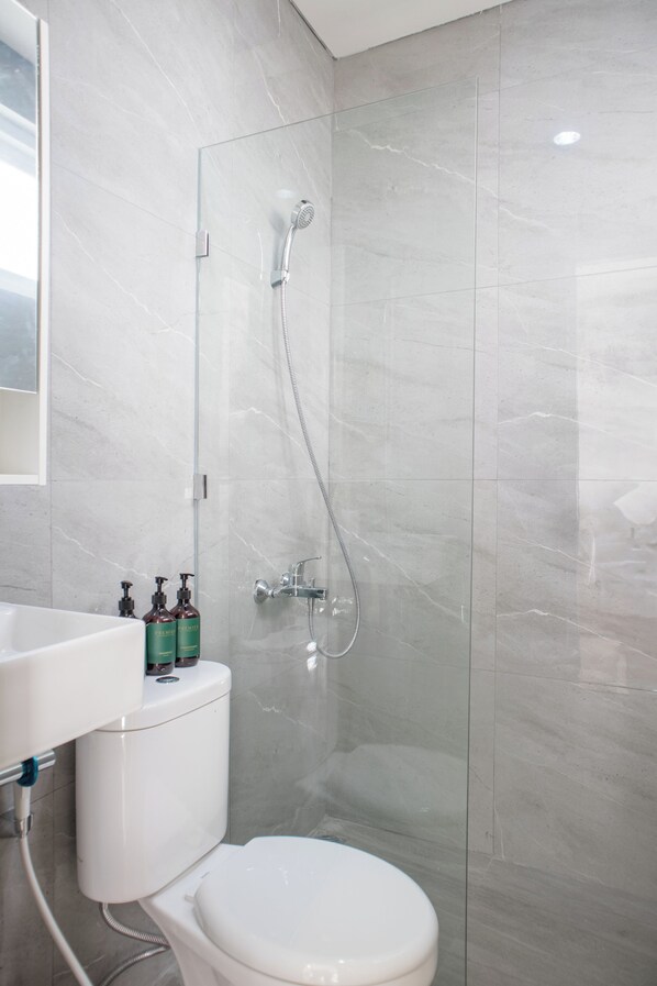 Une salle de bain moderne avec une douche à parois de verre, des toilettes blanches et un lavabo équipé de distributeurs de savon.