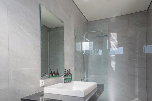 Un baño moderno con un espejo grande, una ducha con cerramiento de vidrio y un lavamanos blanco.