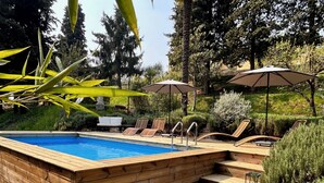 Una terraza de madera con piscina, sillones de descanso y sombrillas.