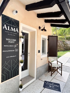 A villa entrance with a digital check-in sign, a welcome mat, and a door leading to a patio area.