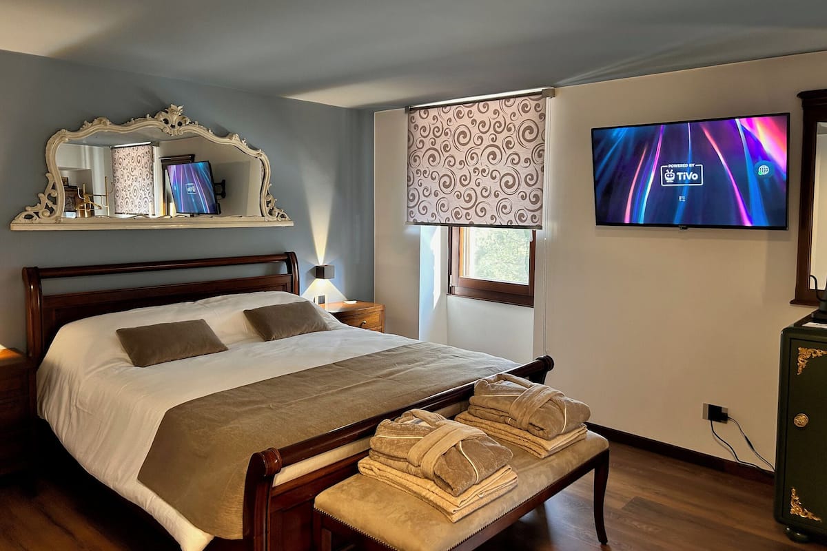 A hotel room with a bed, a TV, a mirror, a window with a view, and a bedside table.