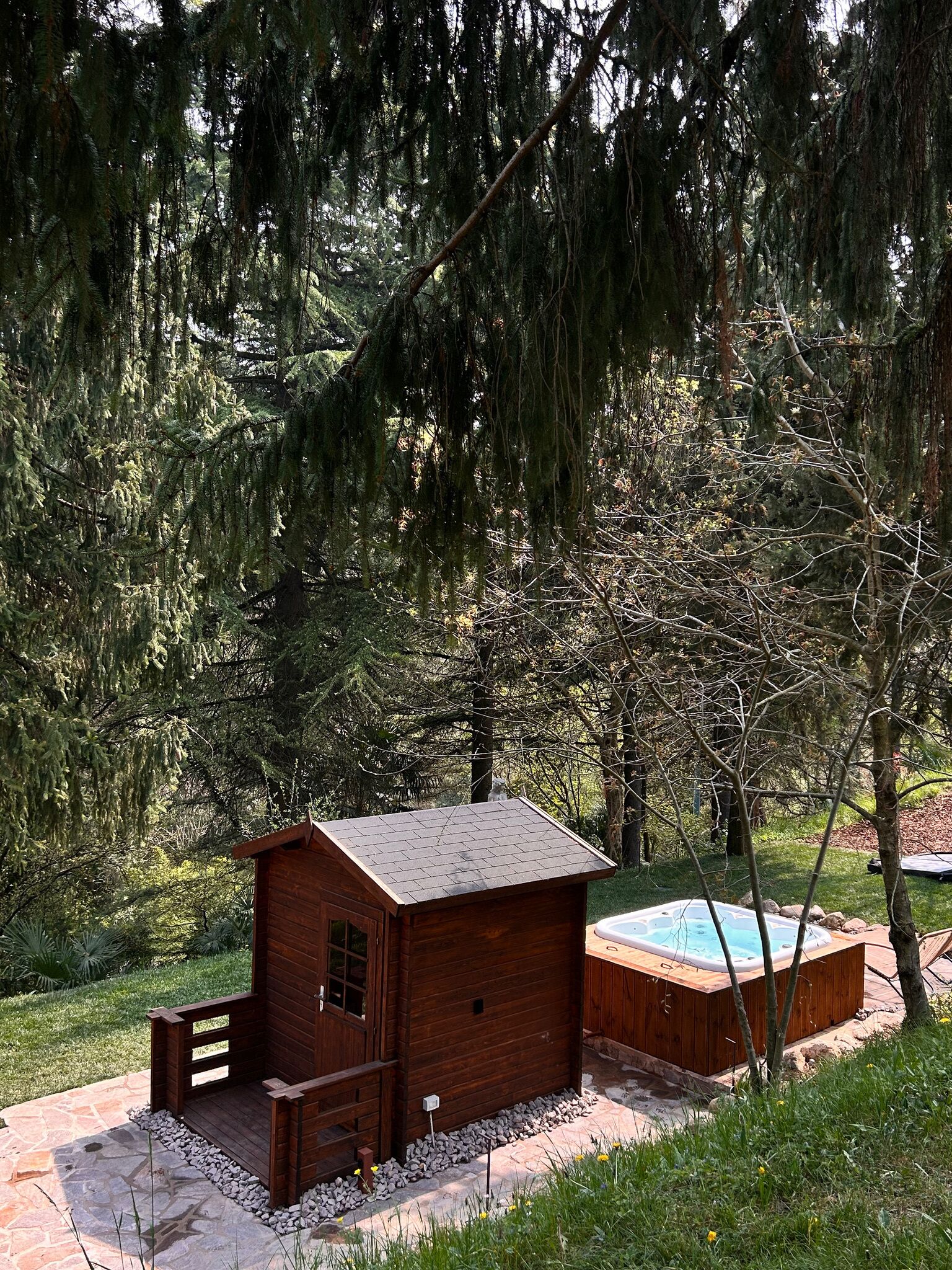 Eine Holzhütte mit einem Steinweg, Bäumen und einem Whirlpool.