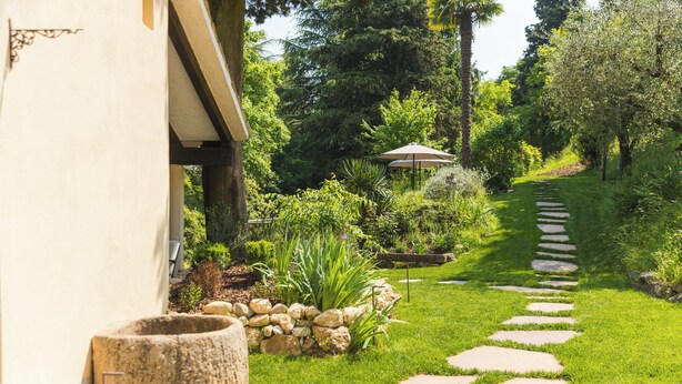 Un sendero de jardín con piedras, un muro de piedra y una zona de patio con sombrilla.
