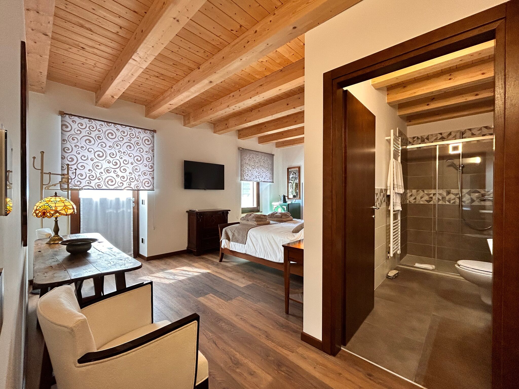Une pièce avec un plafond en bois, un lit, une télévision, une table avec une lampe et un espace douche.