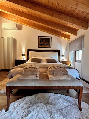 A bedroom with a wooden ceiling, a bed with pillows, a bedside table, a radiator, and a window with a blind.