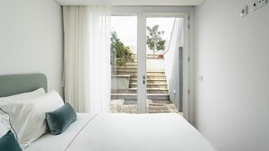 A modern bedroom with a large bed, a view of a garden through a sliding door, and a clean, minimalist design.