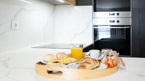 A breakfast tray with croissants, pastries, scrambled eggs, and a glass of orange juice on a white marble countertop in a modern kitchen with a built-in oven.