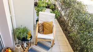 A patio area with a wicker chair, a small table with a book and a cup, and various potted plants. - Haplotēs Rhodes Apartment (Koskinou)