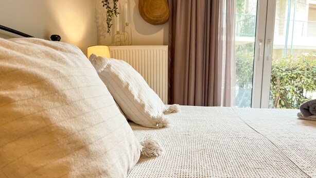 A bed with a textured white cover, a white pillow, and a decorative item on the bed. - Haplotēs Rhodes Apartment (Koskinou)