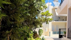 A narrow courtyard with a tiled floor, surrounded by buildings with balconies and potted plants. - Haplotēs Rhodes Apartment (Koskinou)