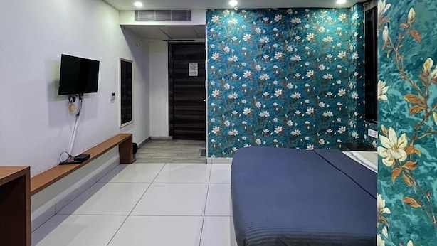 A modern bedroom with a bed, a ceiling fan, a TV, and a floral wallpaper. - Kinsfolk Inn Hotel And Banquet (Ghaziabad)