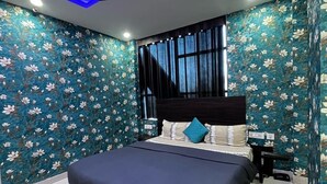 A modern bedroom with a large bed, a ceiling fan, and floral wallpaper. - Kinsfolk Inn Hotel And Banquet (Ghaziabad)