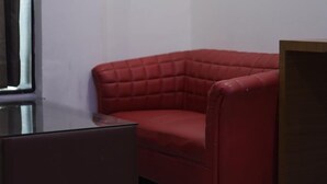 A red sofa in a corner of a room with white walls and a glass table. - Kinsfolk Inn Hotel And Banquet (Ghaziabad)