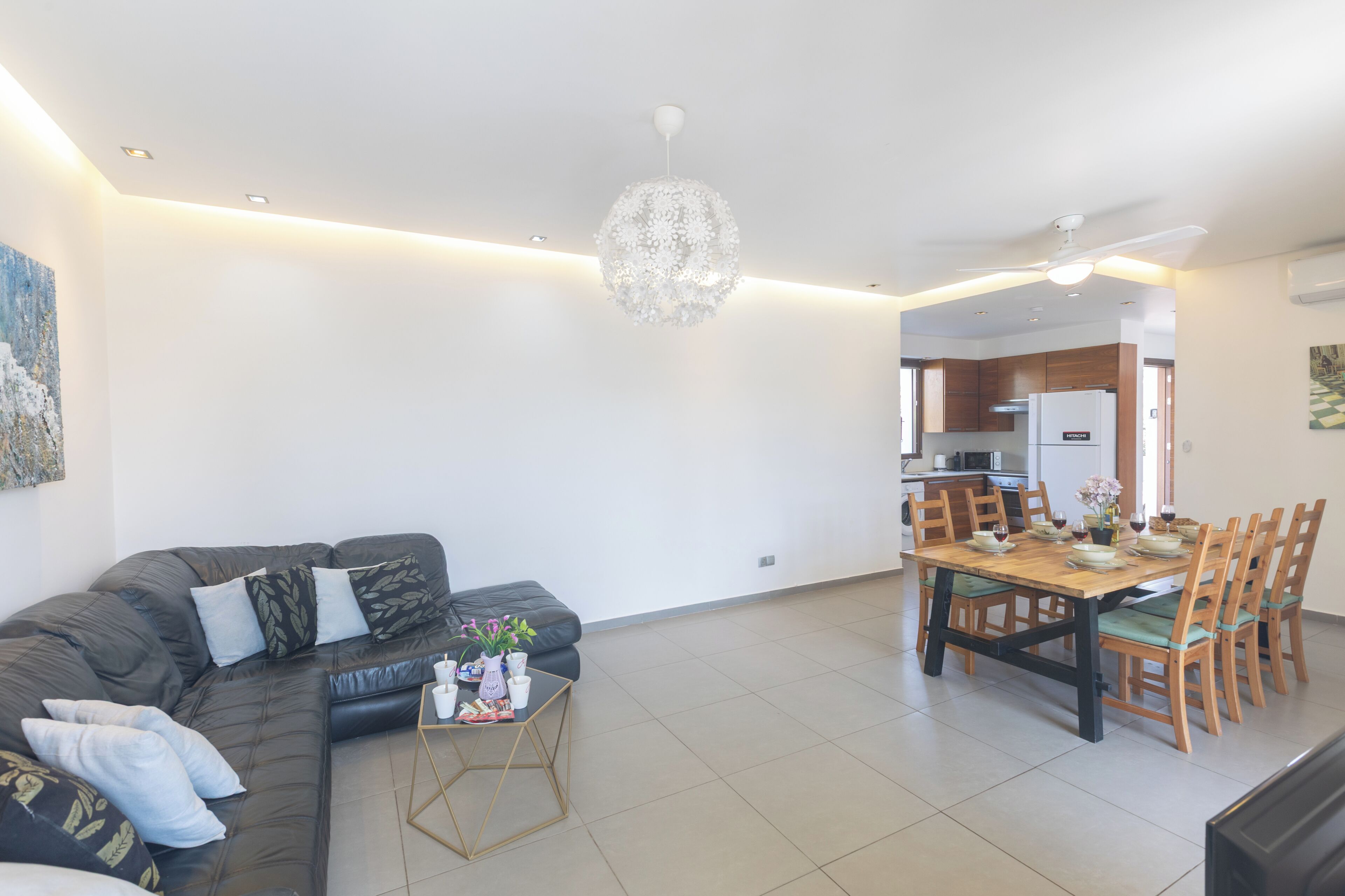 A modern living room with a sectional sofa, a dining table with chairs, and a chandelier.