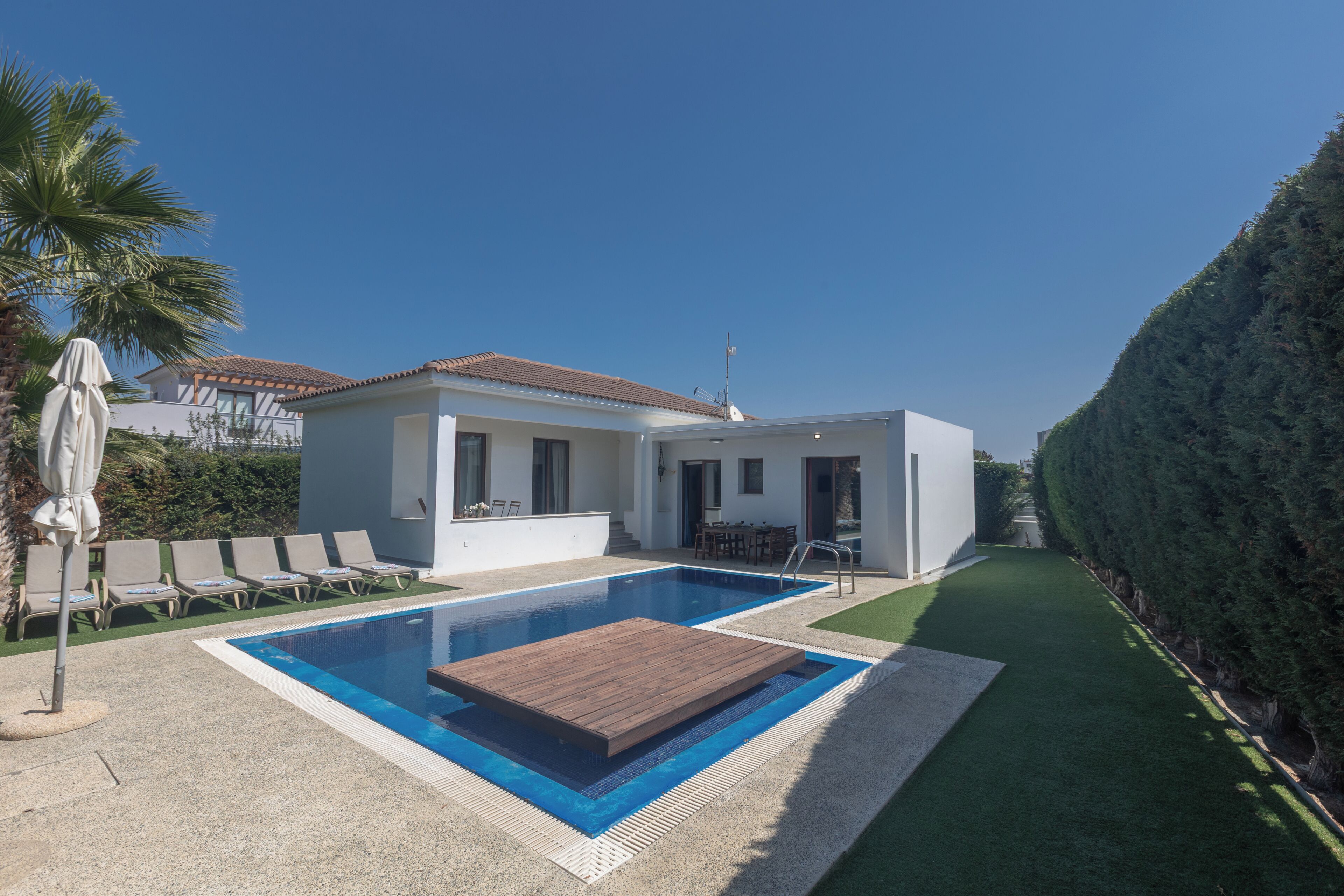 A modern house with a swimming pool, a patio with lounge chairs, and a well-maintained lawn.