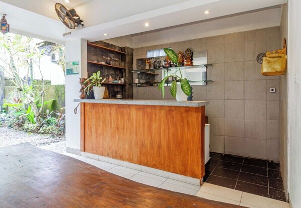 A reception area with a wooden counter, shelves with decorative items, and a potted plant. - Saren Guesthouse by Secoms (Kerobokan)