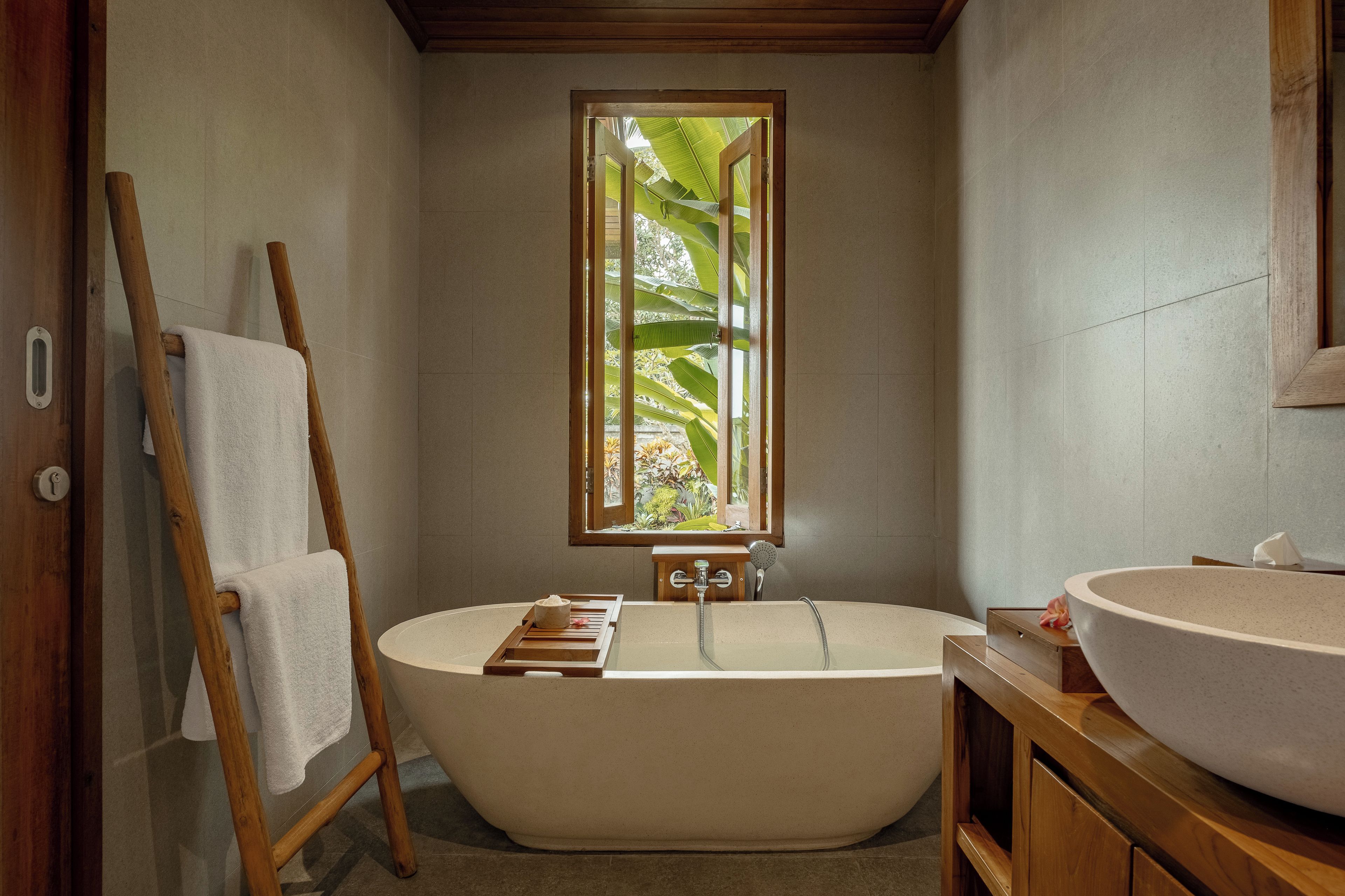 Ein Badezimmer mit einer freistehenden Badewanne, einem Holzbadezimmer-Möbel und einem Fenster mit Blick auf Grünflächen.