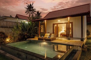 A poolside area with a lounge chair, a small table, and a bedroom visible through an open door.