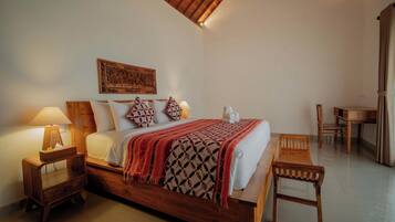 Een houten bed met een bedsprei met patroon, een nachtkastje met een lamp en een houten stoel.