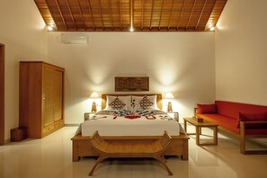 Un dormitorio con una cama, lámparas de noche, un banco de madera, un sofá rojo y un armario de madera.