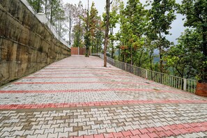 A paved pathway with a metal railing, surrounded by trees and a concrete wall. - PRAKRTI-THE NATURE (Lansdowne)