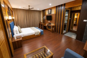 Habitación de hotel con cama, escritorio, televisor y ventilador de techo.