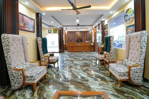 A hotel lobby with a reception desk, two armchairs, a sofa, and a ceiling fan. - PRAKRTI-THE NATURE (Lansdowne)