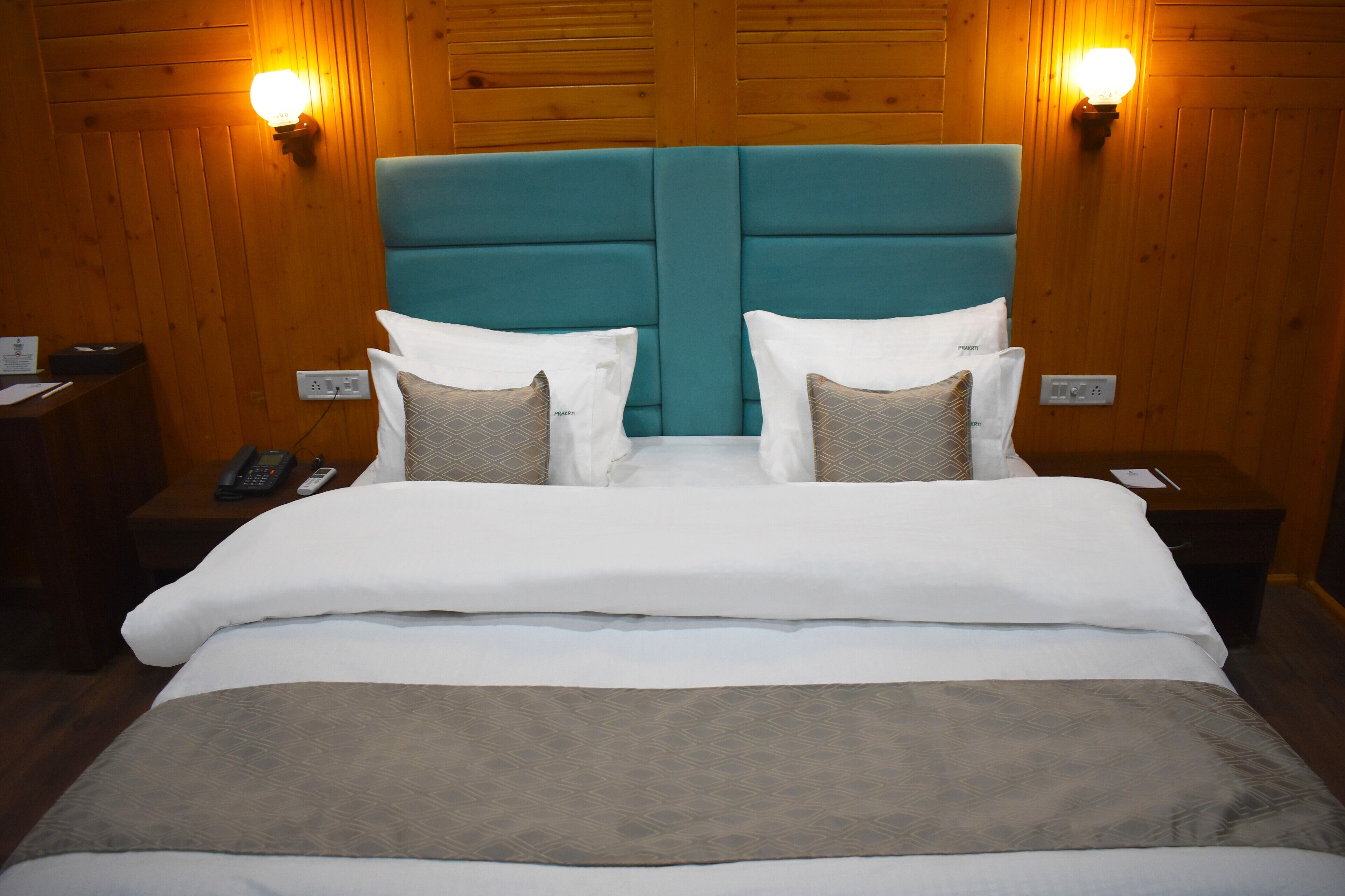 A hotel room with a teal headboard, white bedding, and two bedside lamps.