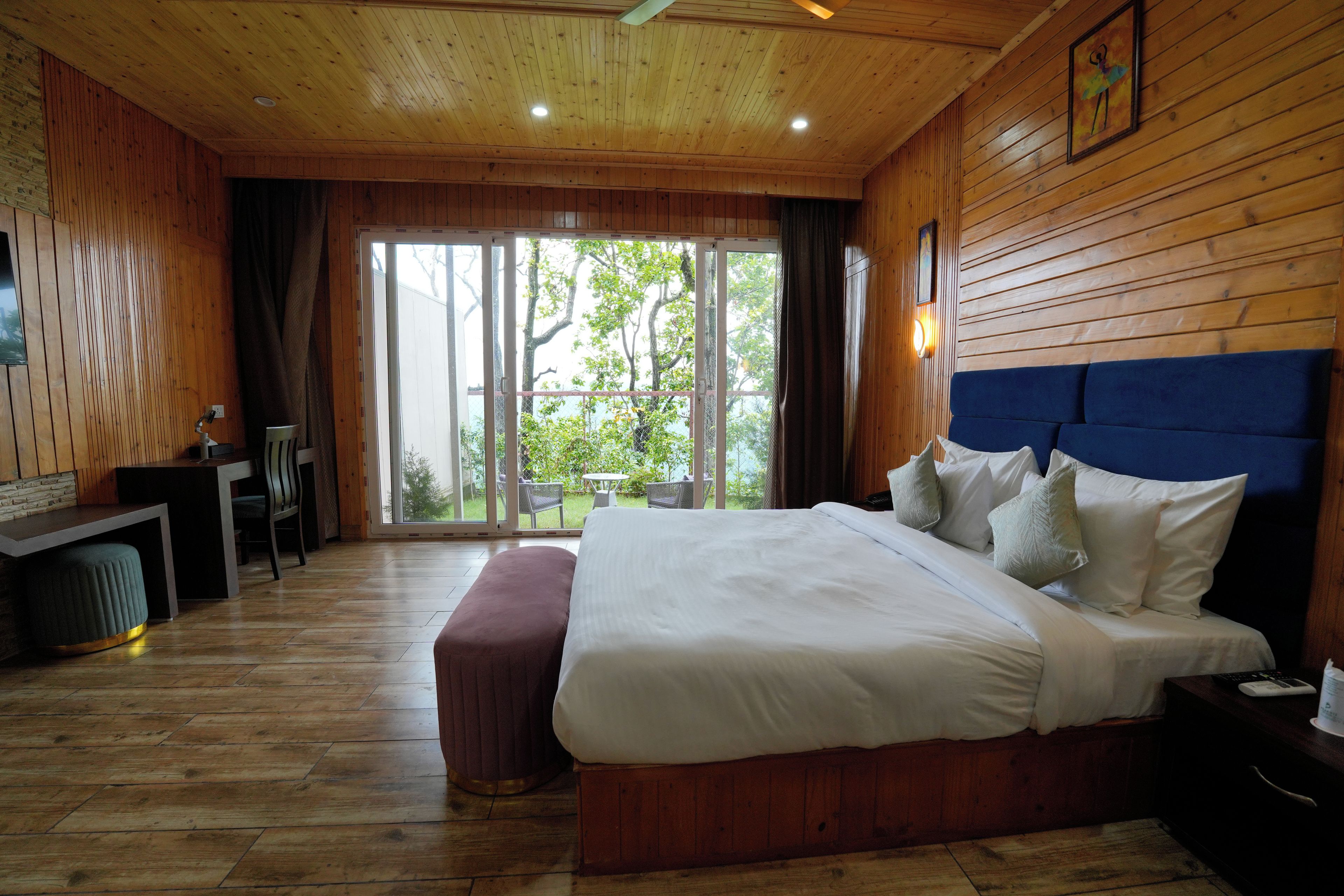 Een kamer met houten lambrisering, een bed, een bank, een bureau en uitzicht door een glazen deur.
