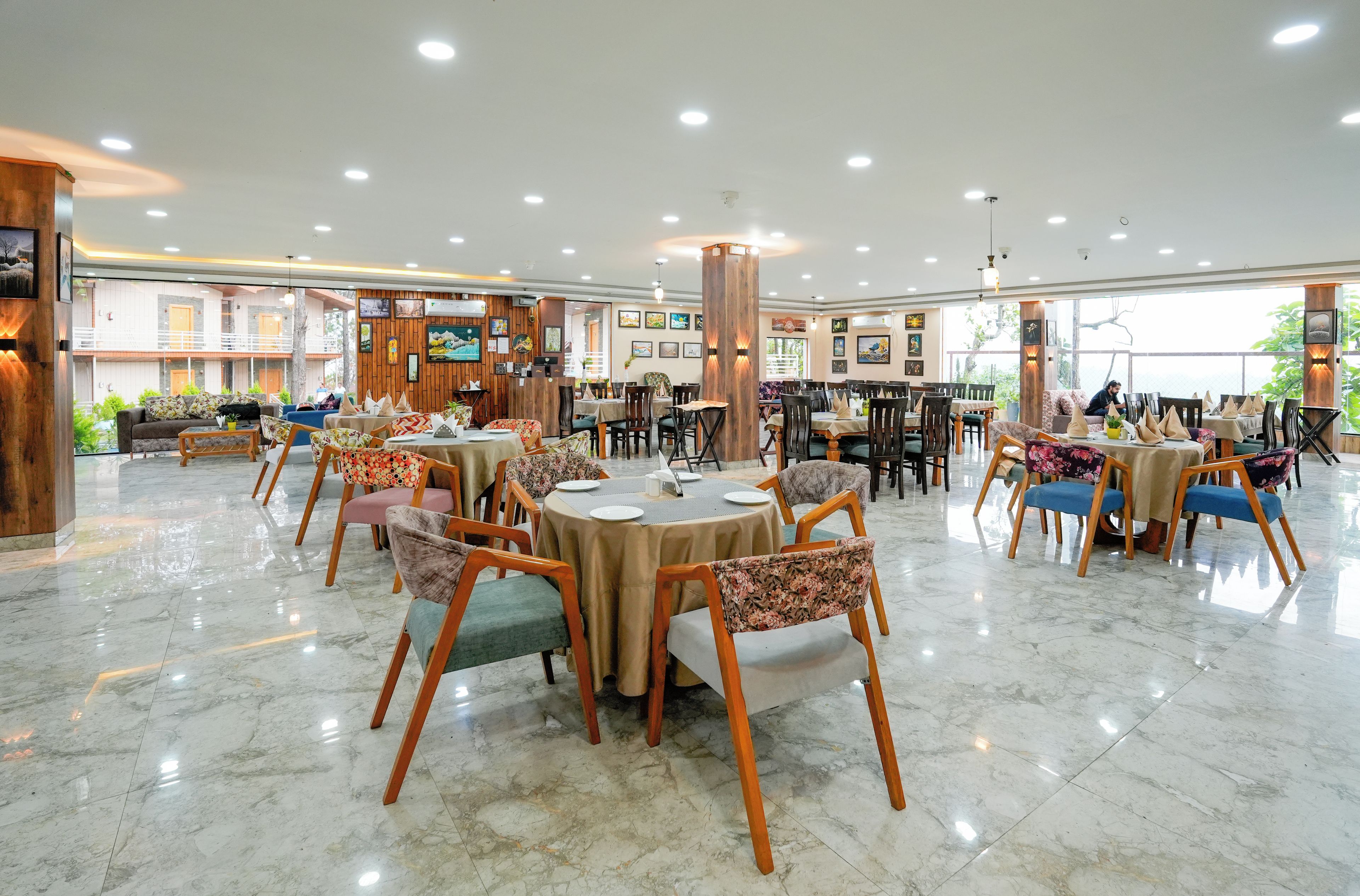 A spacious dining area with multiple round tables and chairs, a wooden reception desk, and a balcony with a view.
