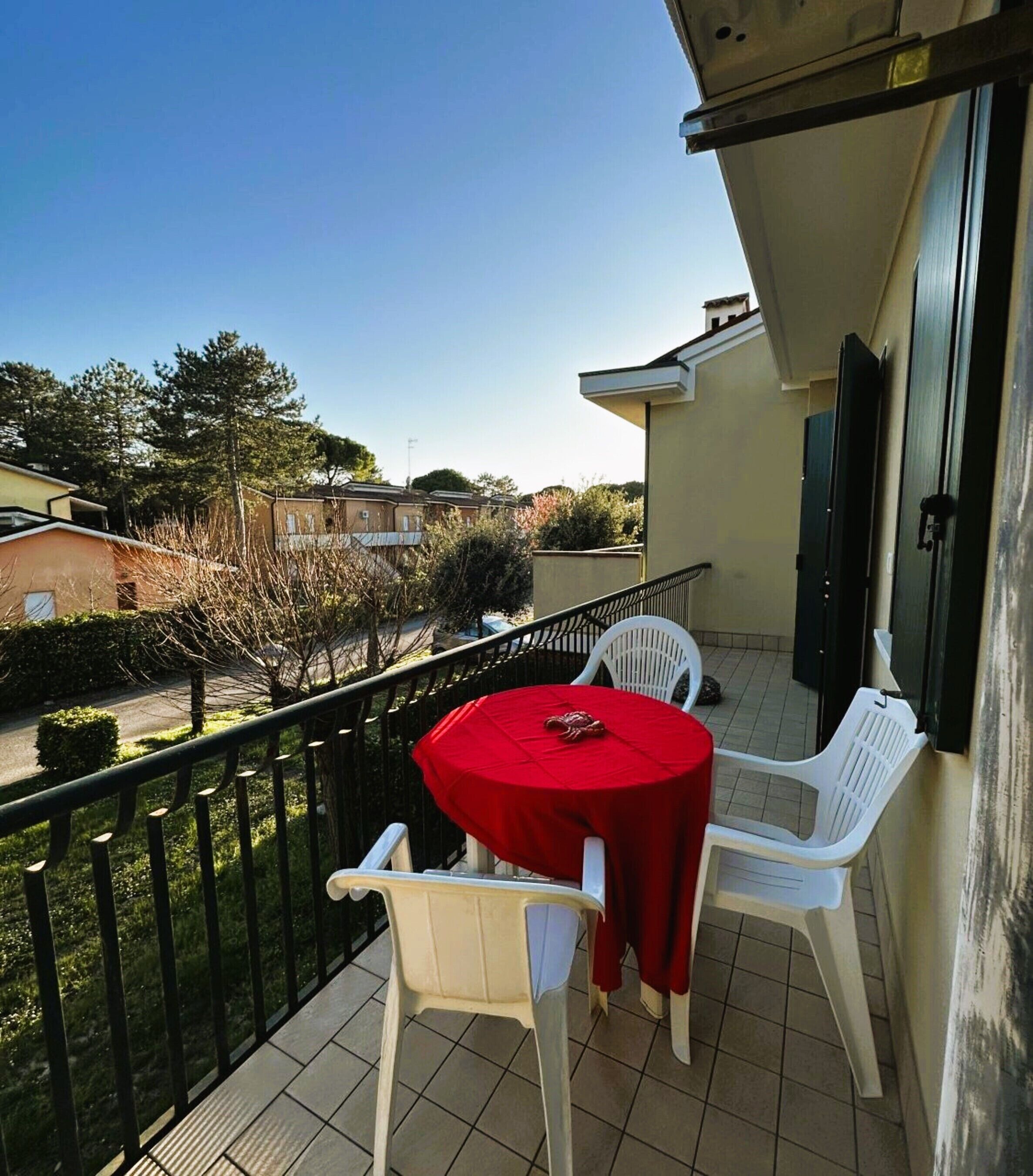 A balcony with a round table and two chairs, a view of the street, and a building in the background.