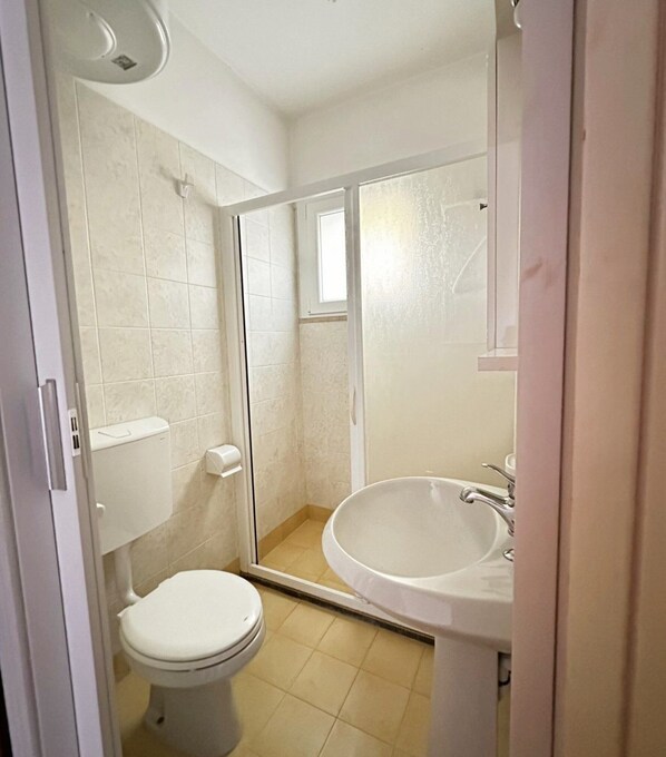 Un baño pequeño con inodoro, lavamanos y cabina de ducha.