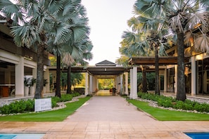 A covered walkway flanked by palm trees leading to a building with a tiled roof.