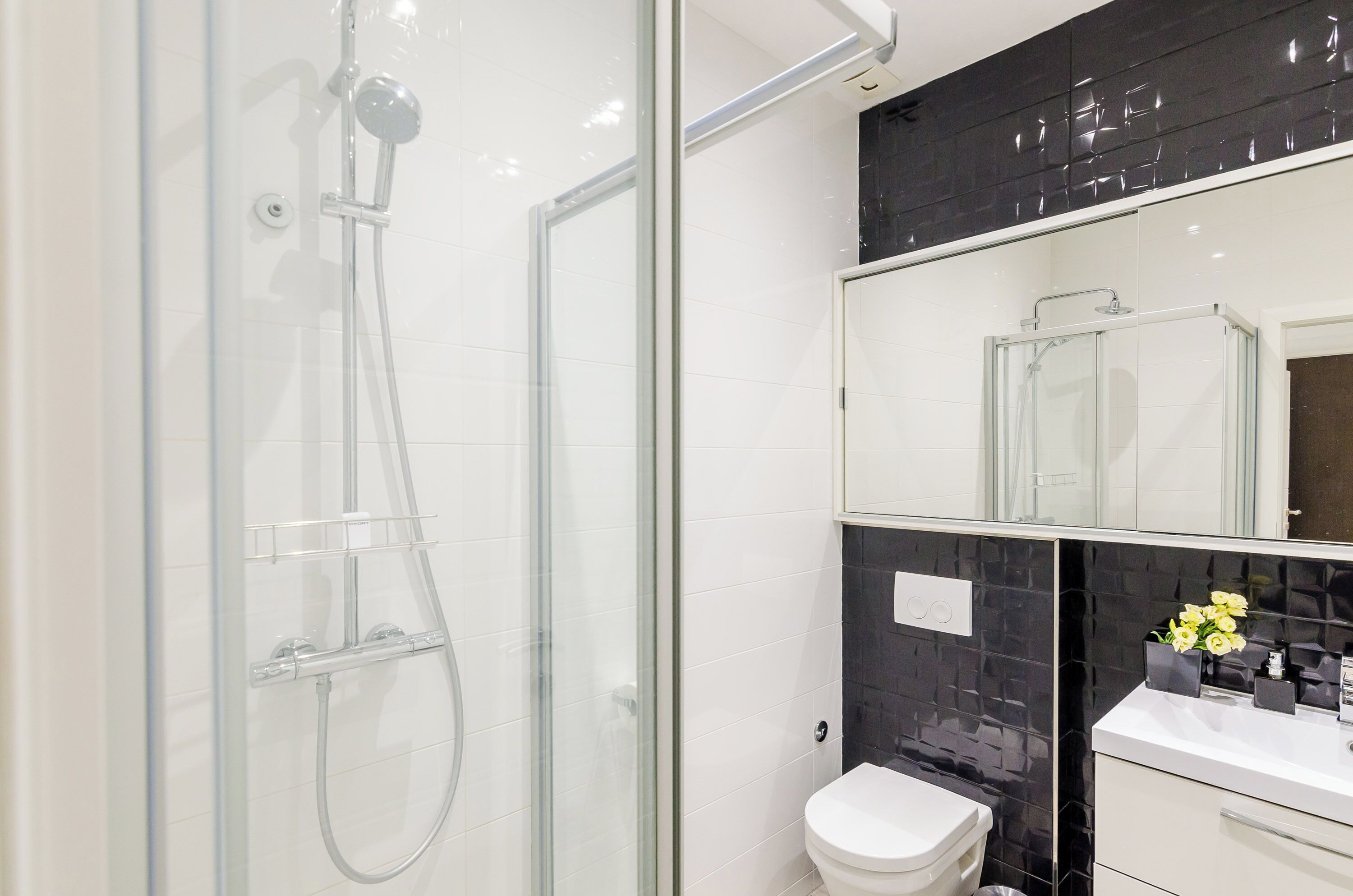 Een moderne badkamer met een douchecabine van glas, een wit toilet en een wastafelmeubel met spiegel en wastafel.