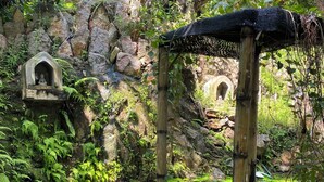 A serene garden with a stone structure, a bamboo pavilion, and a pond with lily pads.